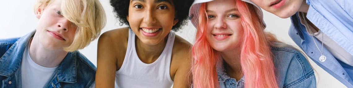 Low angle of group of cheerful multiethnic teenager friends standing together against white background and looking at camera